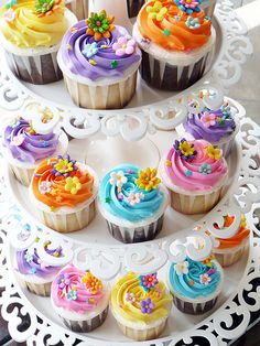 there are many cupcakes that are on the cake platter and it is decorated with colorful icing