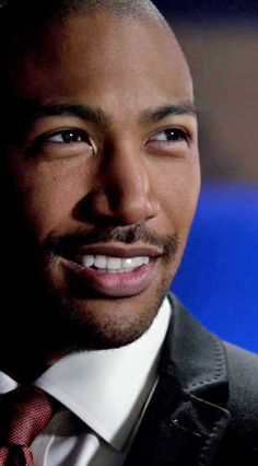 a close up of a person wearing a suit and tie with a smile on his face