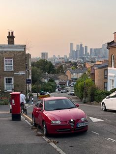 a red car parked on the side of a road next to a mailbox and some buildings