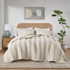 a bed with white comforter and pillows in a bedroom next to a plant on the floor