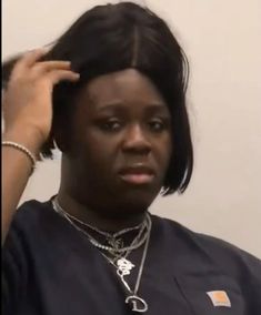 a woman is getting her hair styled by another woman in the background, wearing a black shirt and bracelets