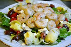 a salad with shrimp and olives on it is sitting on a white paper plate