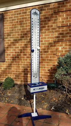 a large metal thermometer sitting on top of a stand in front of a brick building