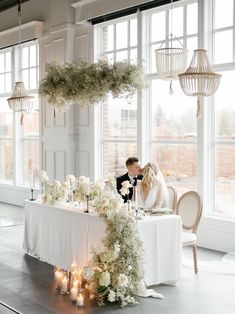 a bride and groom kissing at their wedding reception table with flowers on the table in front of them