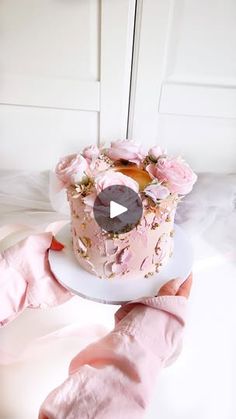 a person is holding a cake with pink frosting and flowers on it, in front of a white door