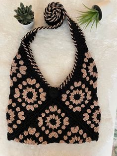 a crocheted black and pink purse sitting on top of a white table next to a potted plant