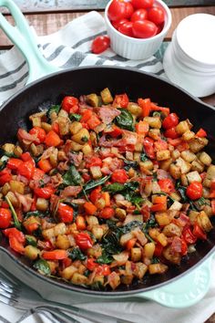 a skillet filled with cooked vegetables on top of a table next to bowls of tomatoes