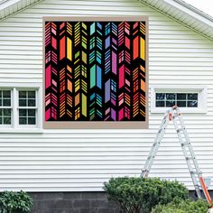 a painting hanging on the side of a white house next to a ladder and window