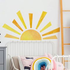 the sun is painted on the wall next to a bed with pink and yellow pillows