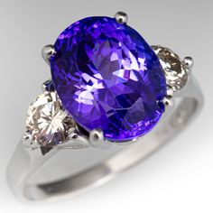 This stunning ring is centered with one (1) oval cut natural tanzanite set into a four-prong setting. The shoulders of the ring are each accented with one (1) prong set round brilliant cut diamond. The ring measures 11.9mm at the top and rises 9.6mm above the finger, tapering to 2.1mm wide and 1.1mm thick at the base of the shank. It currently fits a size 8.75. There is a small scratch on the surface of the tanzanite but it does not detract from the overall magic of the stone. Luxury Tanzanite Ring With Bezel Setting, Luxury Tanzanite Rings With Tension Setting, Luxury Tanzanite Necklaces With Prong Setting, Brilliant Cut Tanzanite Gemstones, Oval Tanzanite Gemstones In Prong Setting, Exquisite Oval Tanzanite Rings, Elegant Tanzanite Gemstones Gia Certified, Classic Sapphire Rings In Purple, Elegant Oval Tanzanite Gemstones