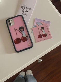 a pink phone case with cherries on it sitting next to a card and some cards