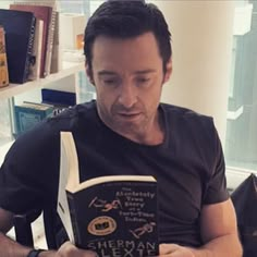 a man reading a book while sitting in front of a table with books on it