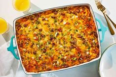 a casserole with meat and vegetables in a blue dish next to two glasses of orange juice