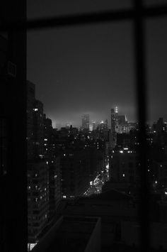 the city lights are lit up at night in black and white, as seen through a window