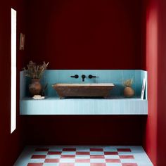 a bathroom with red walls and checkered flooring, two sinks in the center