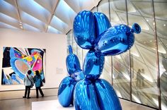 a blue balloon dog sculpture sitting on top of a white pedestal in front of a glass wall