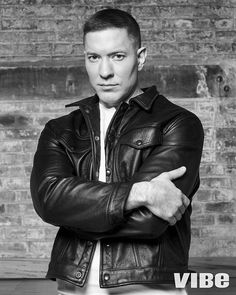 a black and white photo of a man in a leather jacket with his arms crossed