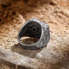 a silver ring sitting on top of a stone slab covered in dirt and sand, with an intricate filigree design