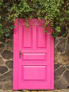 a bright pink door with ivy growing over it's top and bottom part, in front of a stone wall