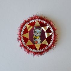 a red and gold ornament with a cat on it's face in the center