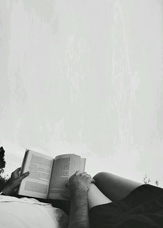 a woman laying on top of a bed holding an open book in her hands and reading it