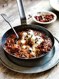 a skillet filled with meatballs covered in sauce and sour cream on top of a wooden table