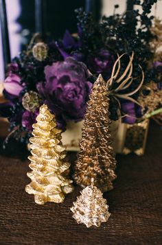 three gold christmas trees sitting on top of a table next to purple and white flowers