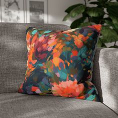 a colorful floral pillow on a gray couch in front of a potted green plant