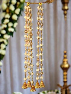 two gold bells hanging from a chandelier with white flowers in front of it