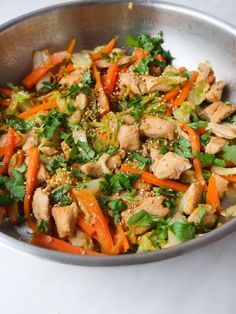 a silver bowl filled with chicken and veggies on top of a white table