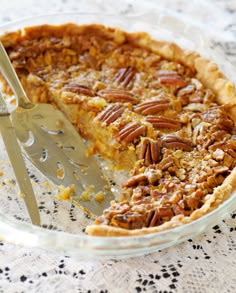 a pie with pecans on top is in a glass dish and has a slice taken out