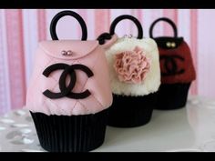 three cupcakes decorated like chanel purses on a white table with pink and black decorations