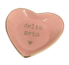 a pink heart shaped dish with the words delta zeta in gold lettering on it