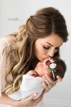 a woman holding a baby in her arms and kissing it's face with the other hand