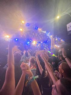 a group of people holding their hands up in the air at a music concert with lights on