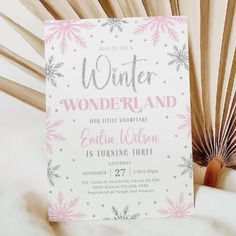 a pink and silver snowflake winter wonderland birthday party card on top of a fan