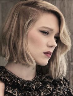 a woman with blonde hair wearing a black dress and looking off to the side while standing in front of a wooden wall