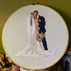 a bride and groom cross stitched together in an embroidery hoop on a table top