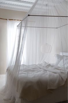 an unmade bed with white sheets and mosquito netting on the headboard, in front of a window