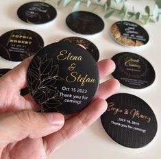 a hand holding a black and gold personalized wedding coasters with leaves on them