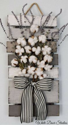 a wooden pallet with cotton flowers tied to it and a bow hanging on the wall