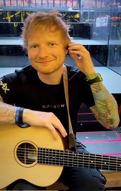 a man sitting in front of a guitar and smiling at the camera with his hand on his head