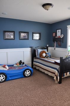 a bedroom with blue walls and carpeted flooring, two cars shaped beds in the middle