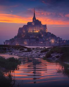 an island with a church lit up at night in the distance and water reflecting off it's surface