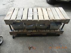 a wooden pallet with four bins on it sitting next to a parked car