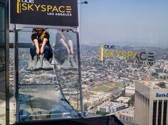 a woman sitting on top of a glass structure in the sky above las angeles, california