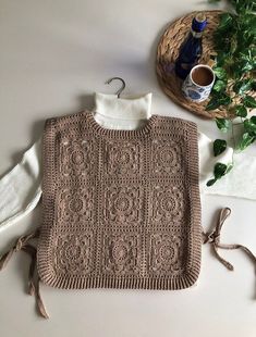 a knitted sweater sits on top of a table next to a potted plant