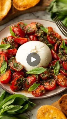 a white plate topped with tomatoes and basil on top of a table next to bread