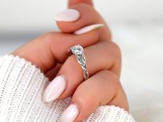 a woman's hand holding a ring with a diamond on it and white nails