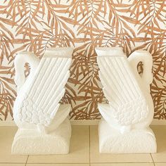 two white vases sitting next to each other on top of a tiled floor in front of a wall